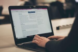 mãos brancas com o braço coberto por mangas pretas digitando em um notebook com uma página de blog corporativo aberta